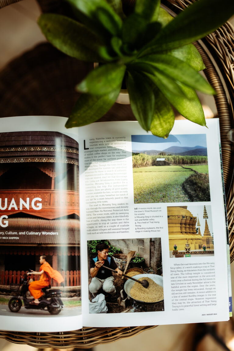 Inspiring travel stories in a magazine at Athena Hotel Pakse, featuring photos of temples, rice fields, and local life in Laos.