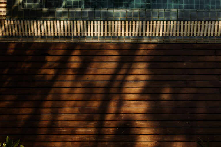 Dappled sunlight creates serene patterns of shadow across the wooden deck by the pool at Athena Hotel Pakse.