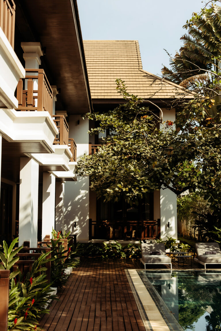 View of the Athena Hotel Pakse building from the poolside, showing its traditional-style balconies and surrounding tropical greenery