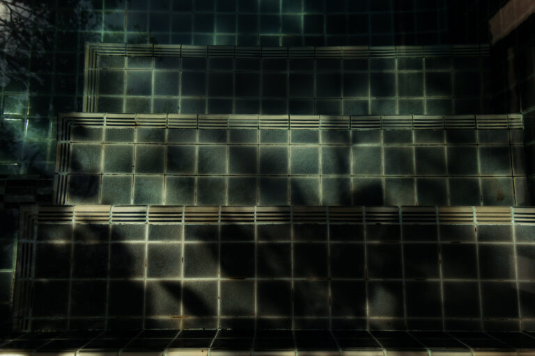 Sunlight and shadows create a beautiful pattern across the tiled underwater steps of the hotel swimming pool.