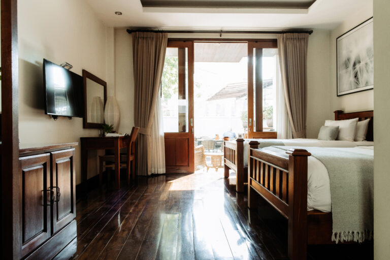 View from inside a hotel room at Athena Hotel Pakse, showing the bed, work desk, and access to a sunlit terrace.