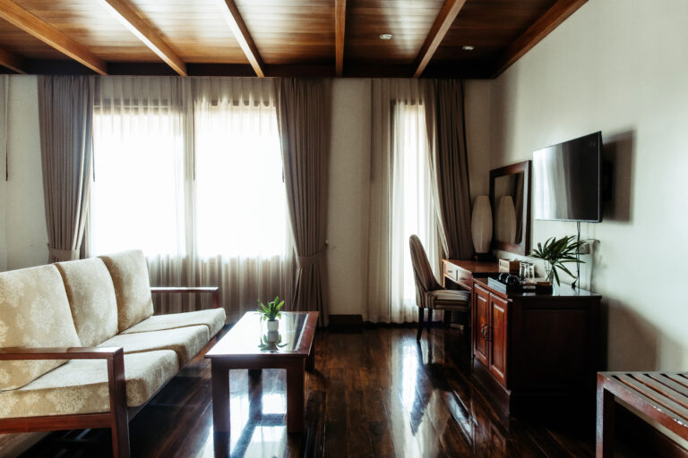 A warm and inviting hotel room interior at Athena Hotel Pakse, featuring dark wood floors, a comfortable sofa, and classic decor.