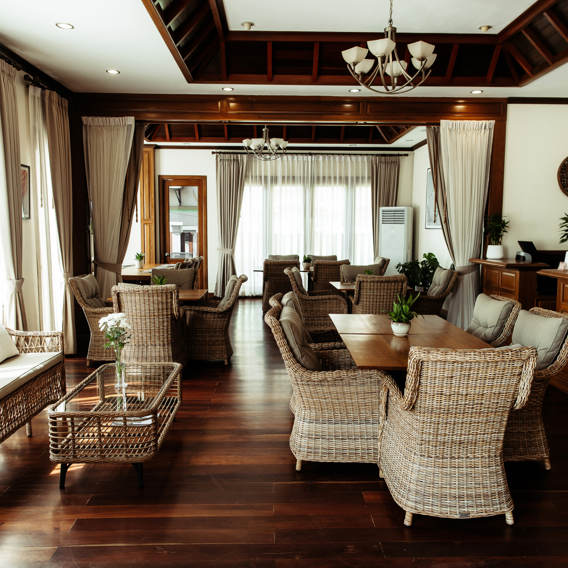 An elegant lounge area featuring classic Indochine decor, with dark wood floors, rattan furniture, and warm lighting