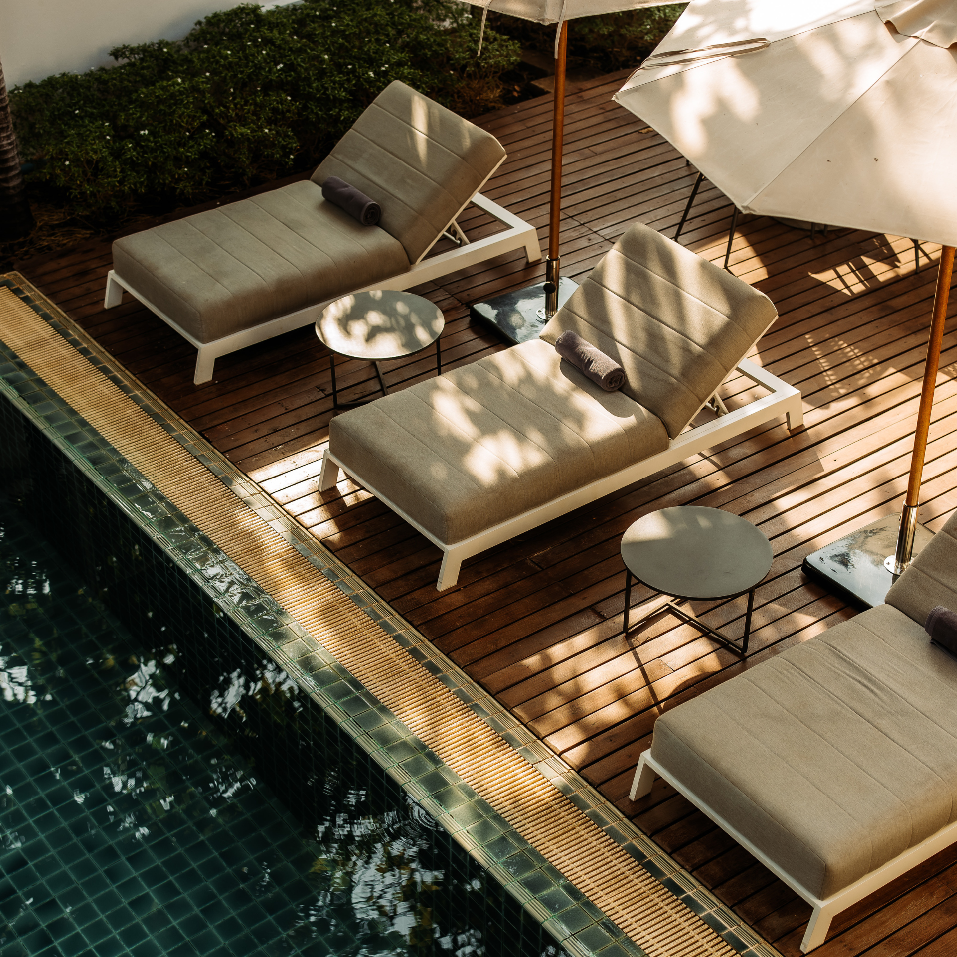 A tranquil poolside scene at Athena Hotel Pakse, with modern sun loungers on a wooden deck under the shade of trees.
